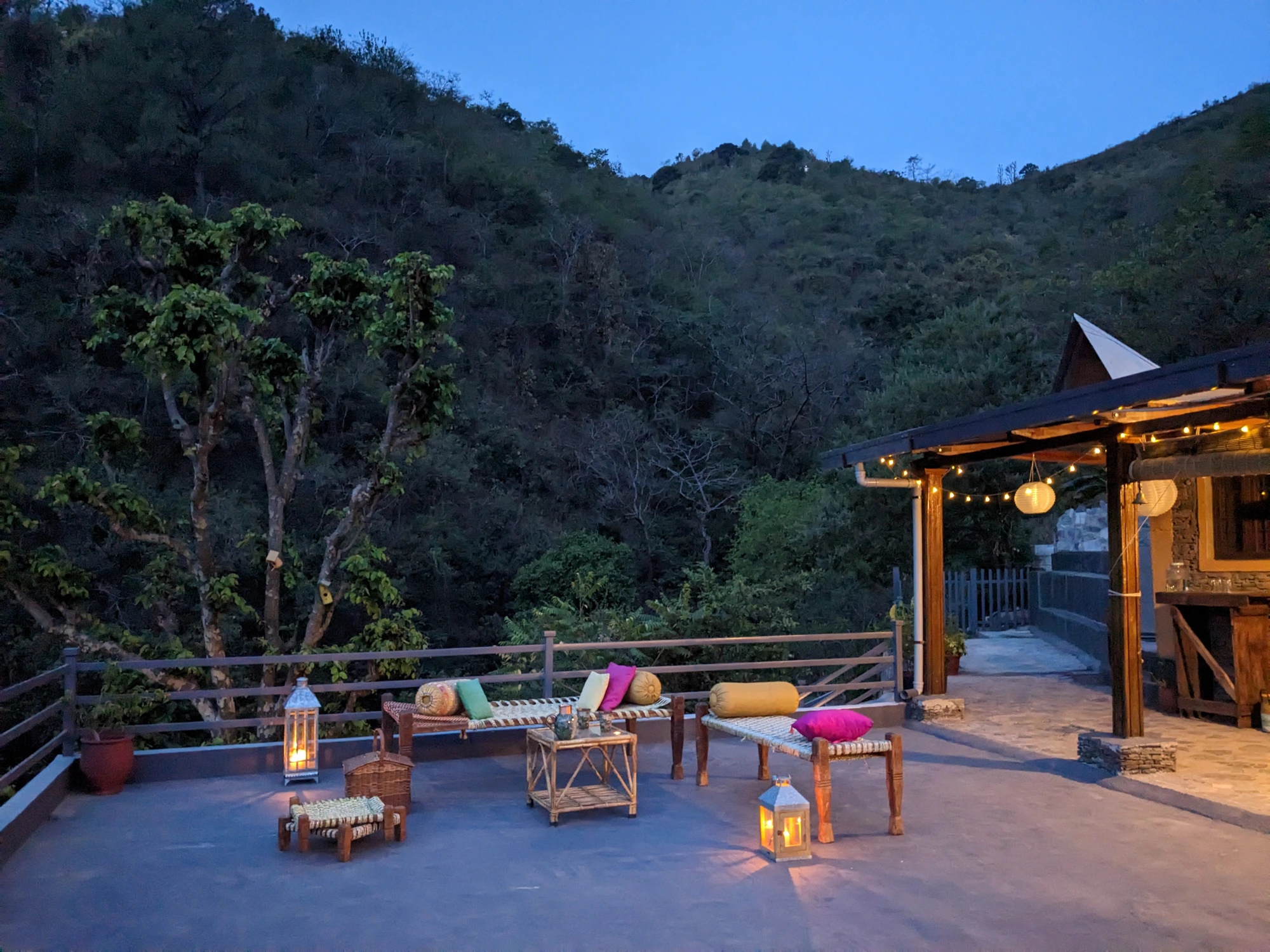 The evening deck with lanterns and charpoys under the hills
